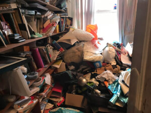Spare room piled high with books, bags and household items before a hoarder house clearance