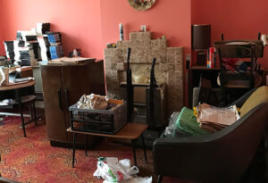 Living room with old furniture, stacked video tapes and newspapers before a house clearance